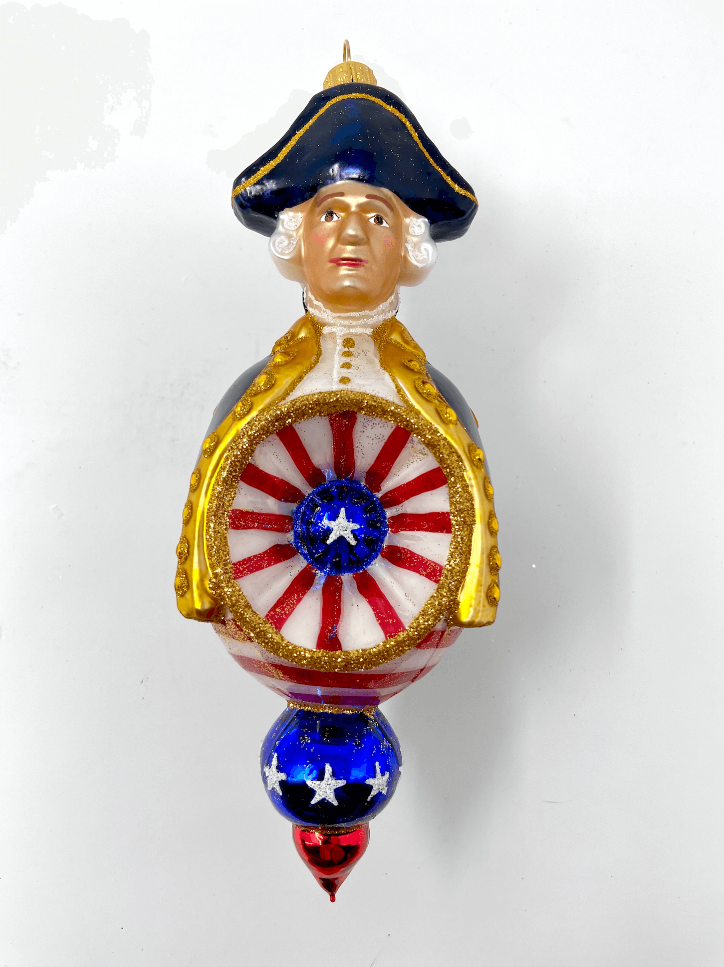 Beautiful George Washington reflector ornament wearing a black cloak and colonial hat with red white and blue patriotic detailing. Polish glass christmas ornaments in saturated colors.