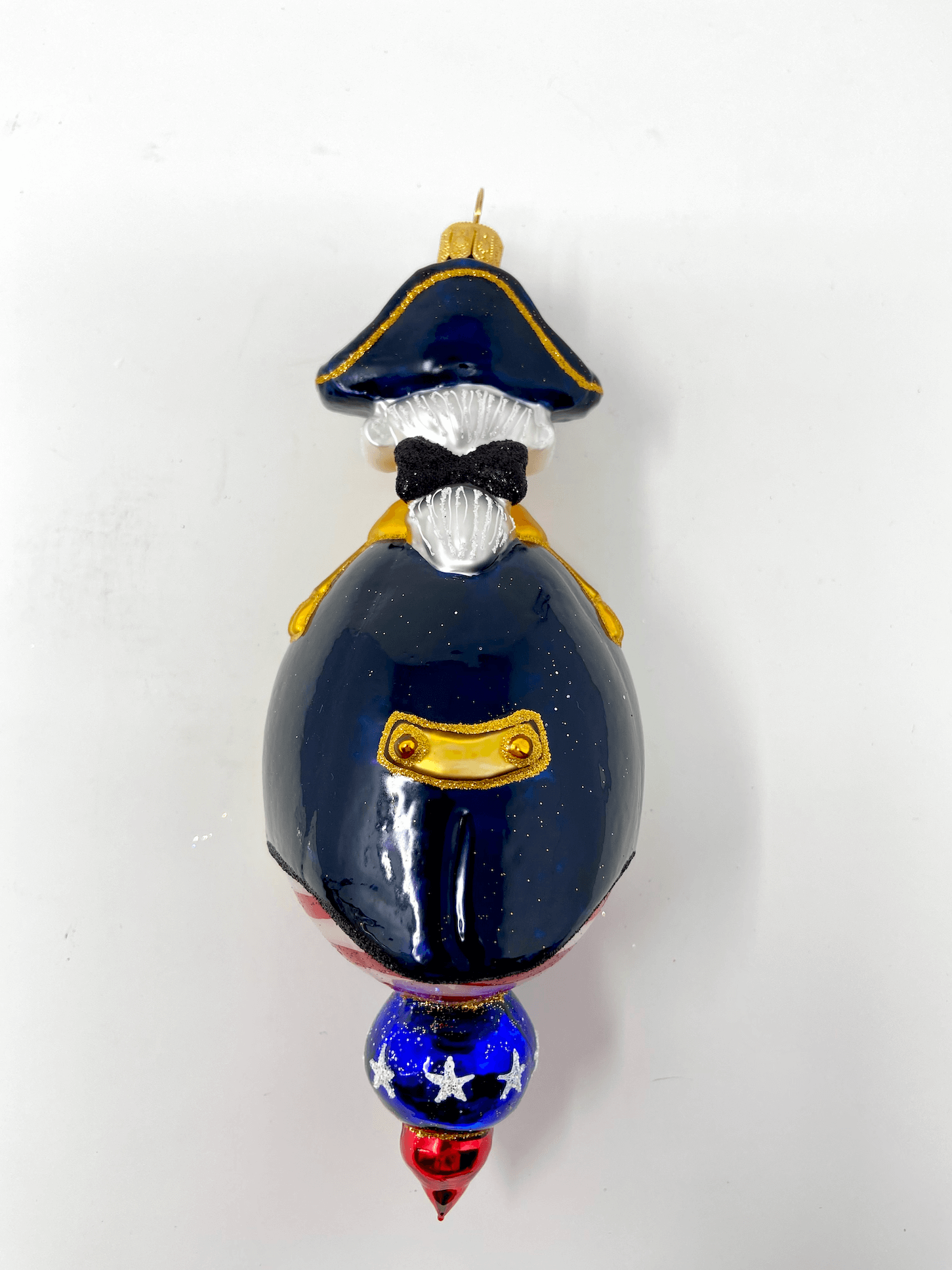 Beautiful George Washington reflector ornament wearing a black cloak and colonial hat with red white and blue patriotic detailing. Polish glass christmas ornaments in saturated colors.
