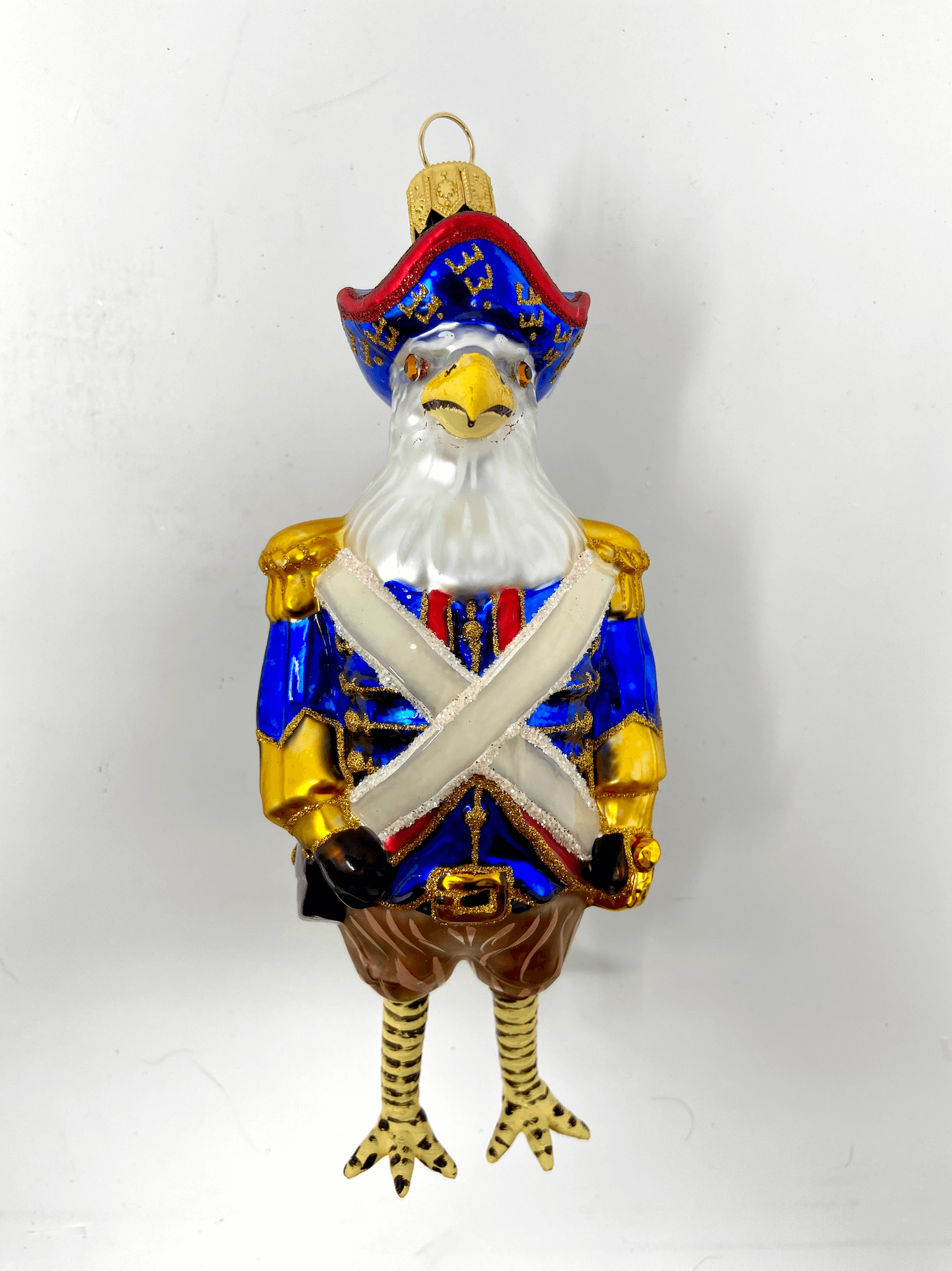 Beautiful and commanding american eagle dressed in a revolutionary war general's blue coat with gilded accents and white sash. Wearing a colonial blue had. Polish glass christmas ornaments in saturated colors.