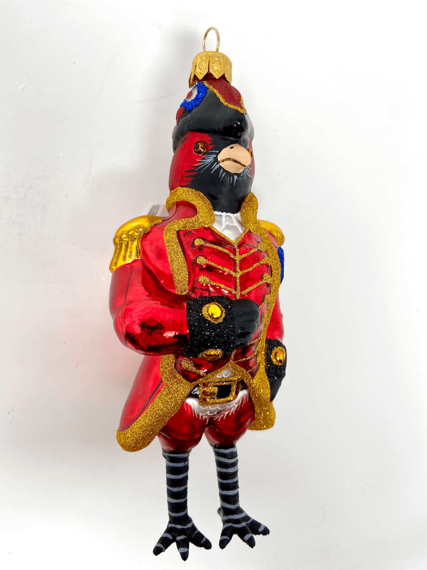 Beautiful red cardinal dressed in a gilded and ornate red English coat and black hat. Polish glass christmas ornaments in saturated colors.